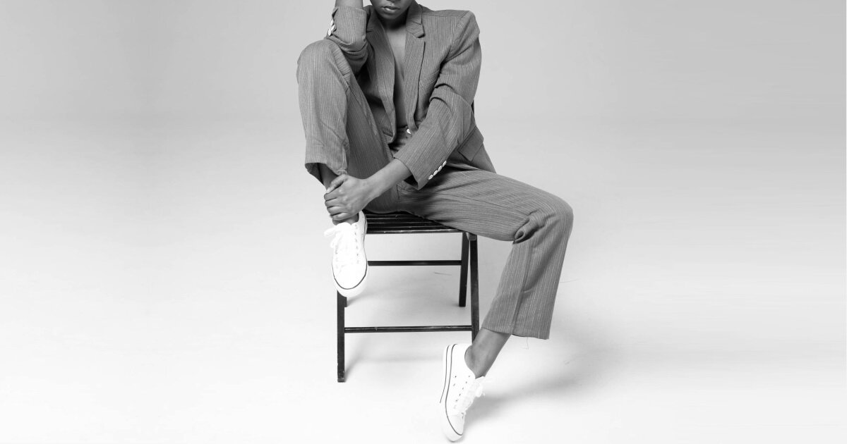 professional woman wears a suit and sneakers; she is sitting on a chair with one leg drawn up.