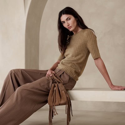 A woman wearing a brown top, darker brown pants, and carrying a brown fringed handbag