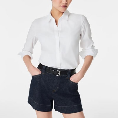 A woman wearing a white long sleeve button-front top and denim shorts with belt