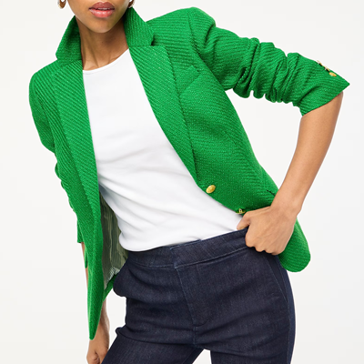 woman wears green tweed blazer, white shirt, and denim pants; her sleeves are scrunched up and she