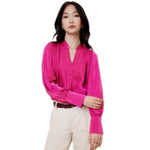 A woman wearing a bright pink blouse, off-white pants, and a brown belt