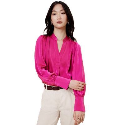 A woman wearing a bright pink blouse, off-white pants, and a brown belt