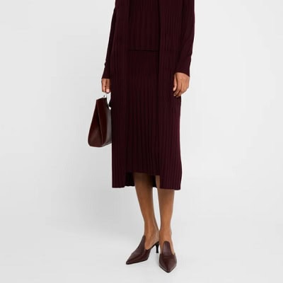 A woman wearing a maroon long cardigan with midi skirt and maroon sandals with maroon handbag