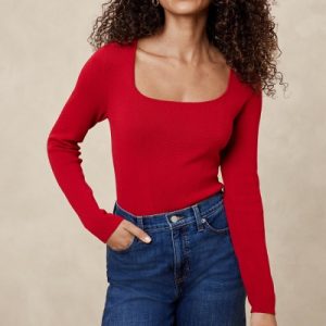 A woman wearing a red long sleeve sweater and denim pants