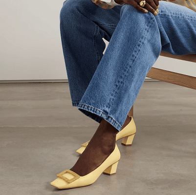 Black woman wears yellow pumps with buckle and slightly curved, low heel