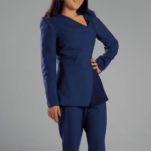 woman wears merino wool peplum blazer with matching suit pants; the blazer has an asymmetrical neckline and a pleated peplum detail on one side in a darker navy (right near where the model has her hand on her hips)