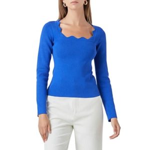 A woman wearing a blue scallop-neck sweater and white pants