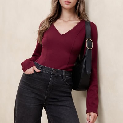 A woman wearing a red long sleeve V-neck top and black pants with black shoulder bag