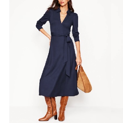 A woman wearing a navy blue long dress with brown high cut boots and brown handbag